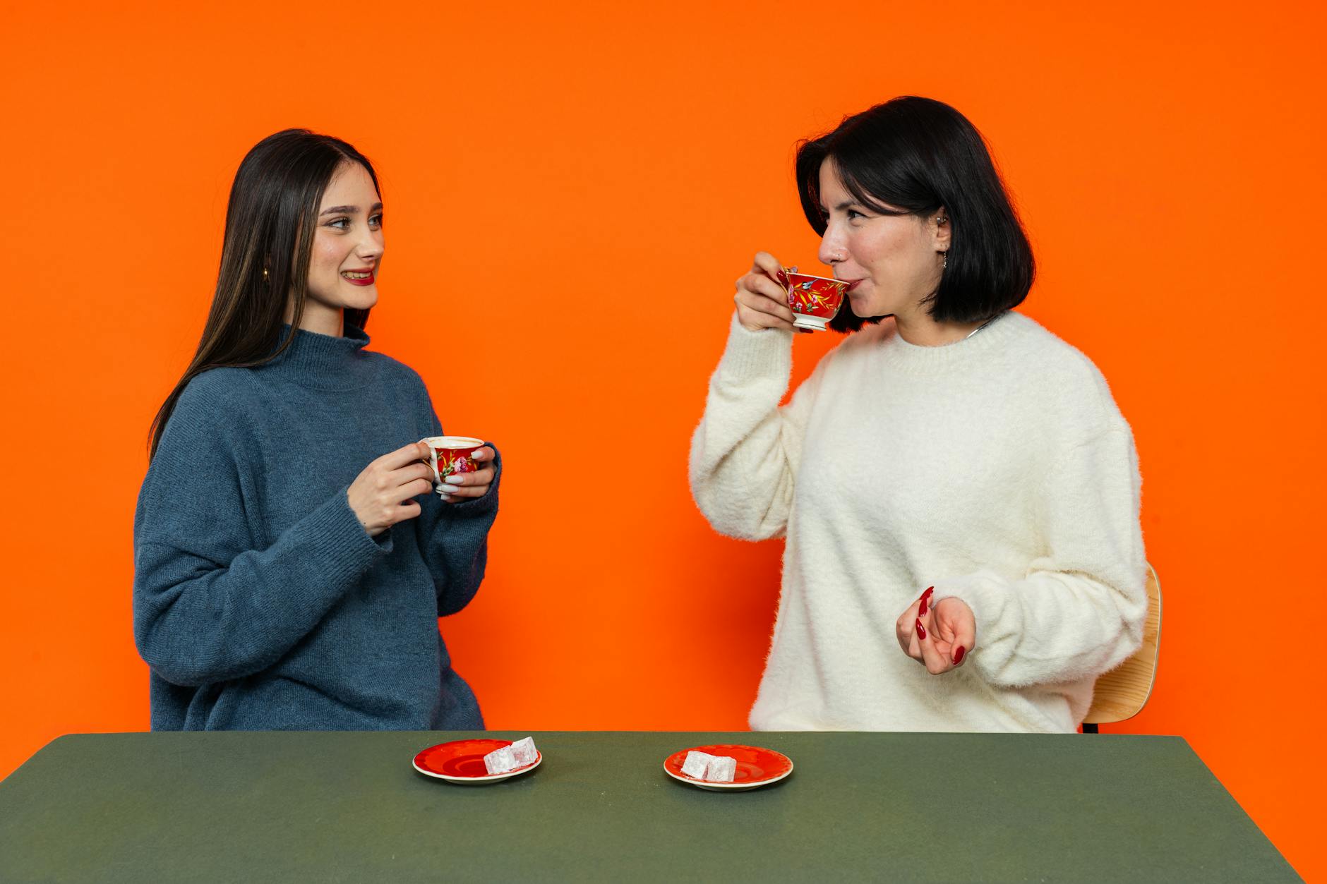 Jak rozmawiać z Turkami: język ciała, małe uprzejmości i rozmowy przy çayu Dwie kobiety piją herbatę i rozmawiają na tle pomarańczowej ściany