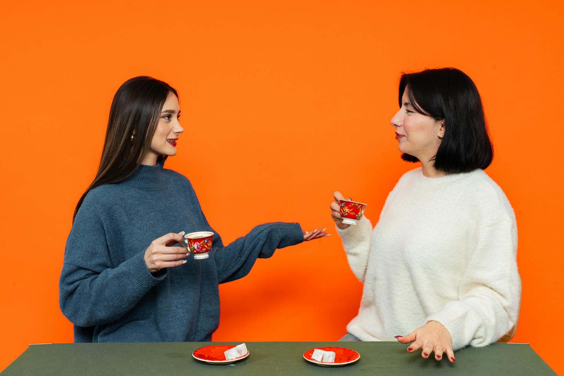 Dwie Turczynki rozmawiają przy herbacie na tle pomarańczowej ściany