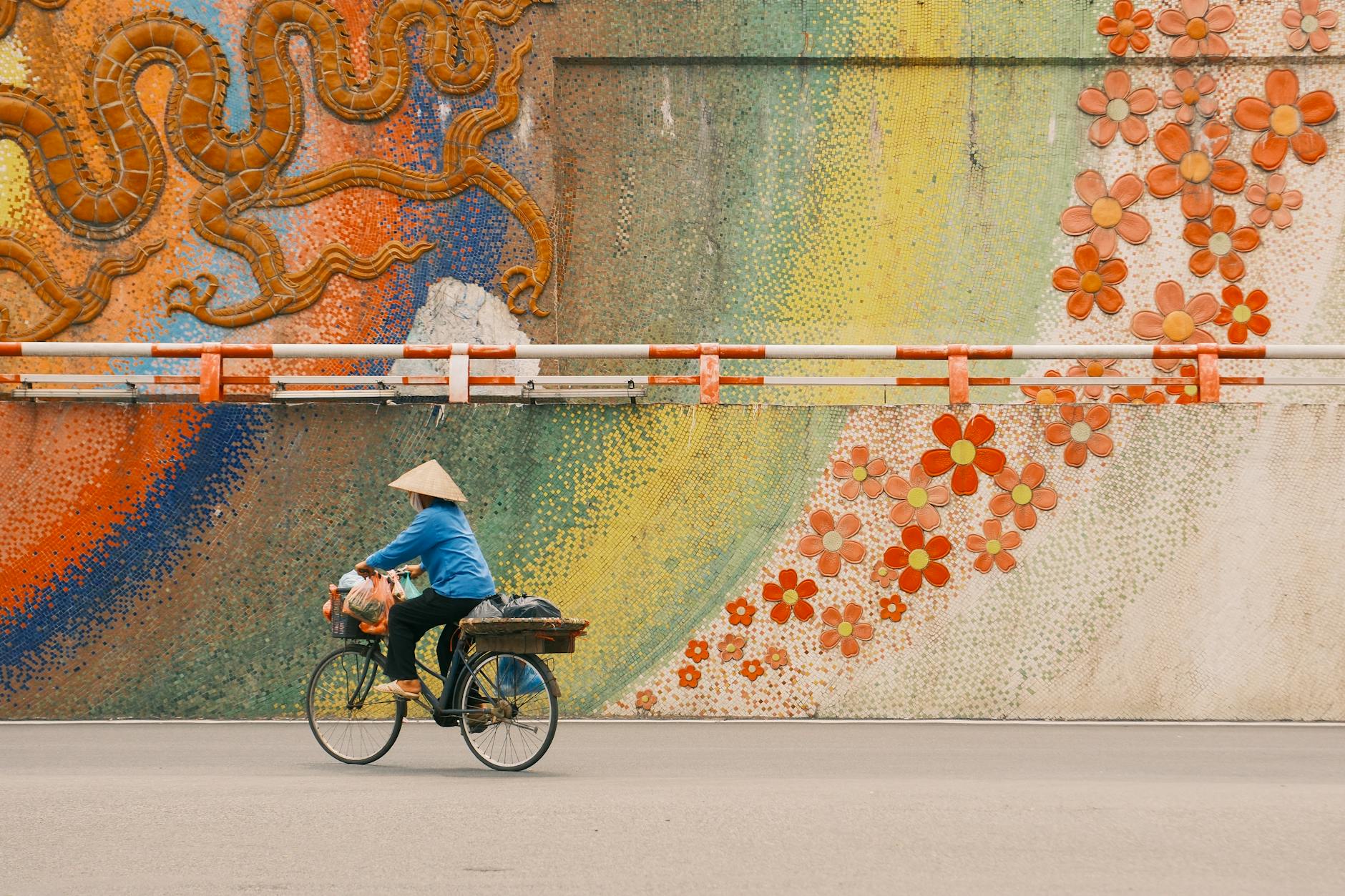 Rowerzysta mija kolorową mozaikę ścienną na ulicy w Hanoi