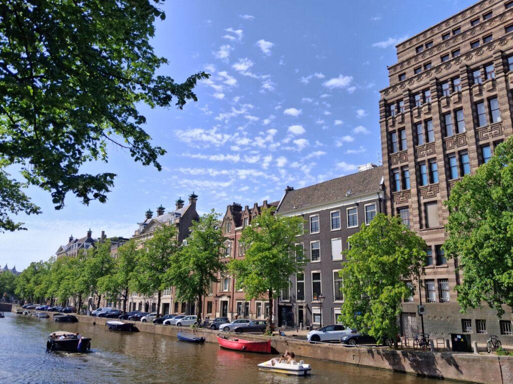 Kanał w Amsterdamie z zabytkowymi kamienicami i drzewami latem